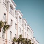 Bright modern building facade with palm trees against a clear blue sky.