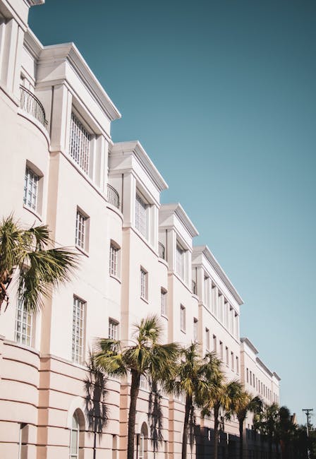 Bright modern building facade with palm trees against a clear blue sky.