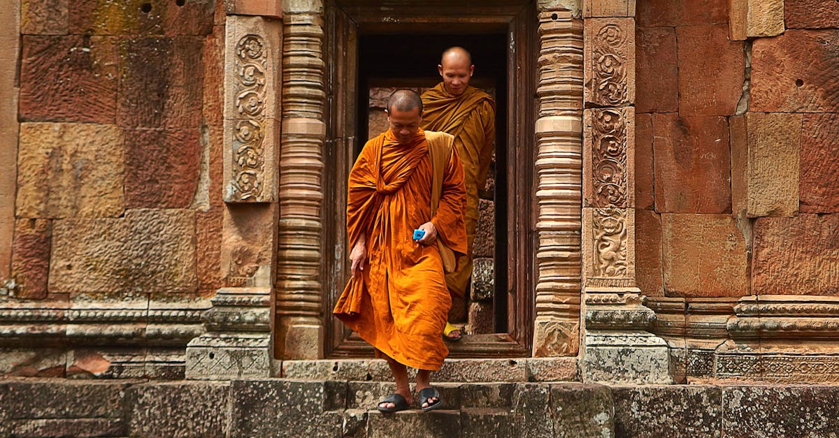 Buddhist monks in orange robes step out of an ancient stone temple in Thailand, showcasing historical architecture.